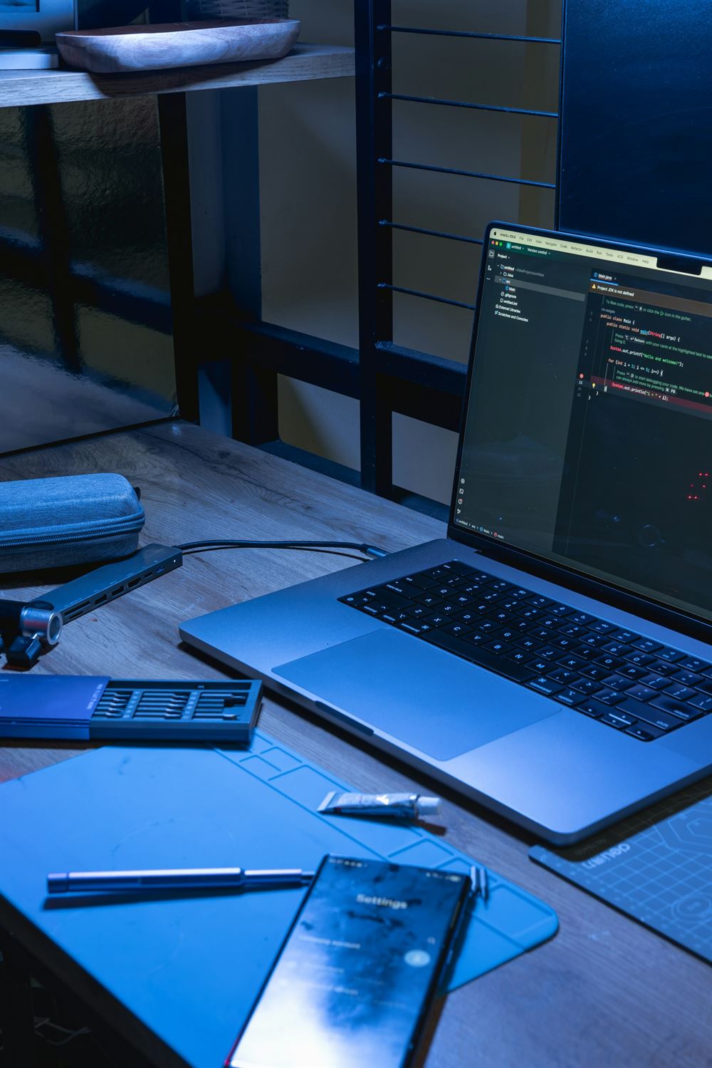 Abends beleuchteter Schreibtisch mit Laptop, auf dem Code im Editor zu sehen ist